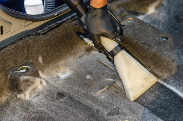 a person using a vacuum to clean the floor of a car